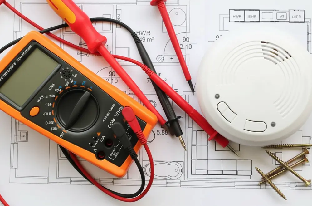 electrical meter and smoke detector on blueprints on a table